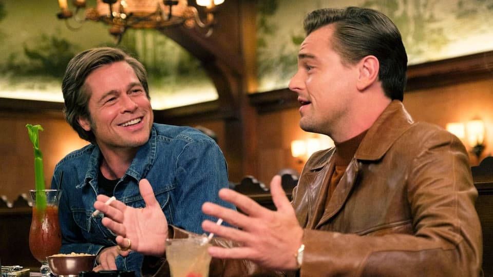 Brad Pitt und Leonardo DiCaprio sitzen in einer Bar und trinken Cocktails.