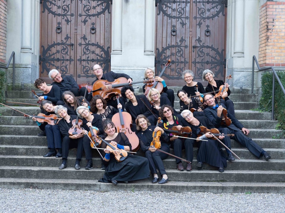 Musikerinnen und Musiker der Orchestrina sitzen auf einer Treppe, alle sind nach links geneigt.