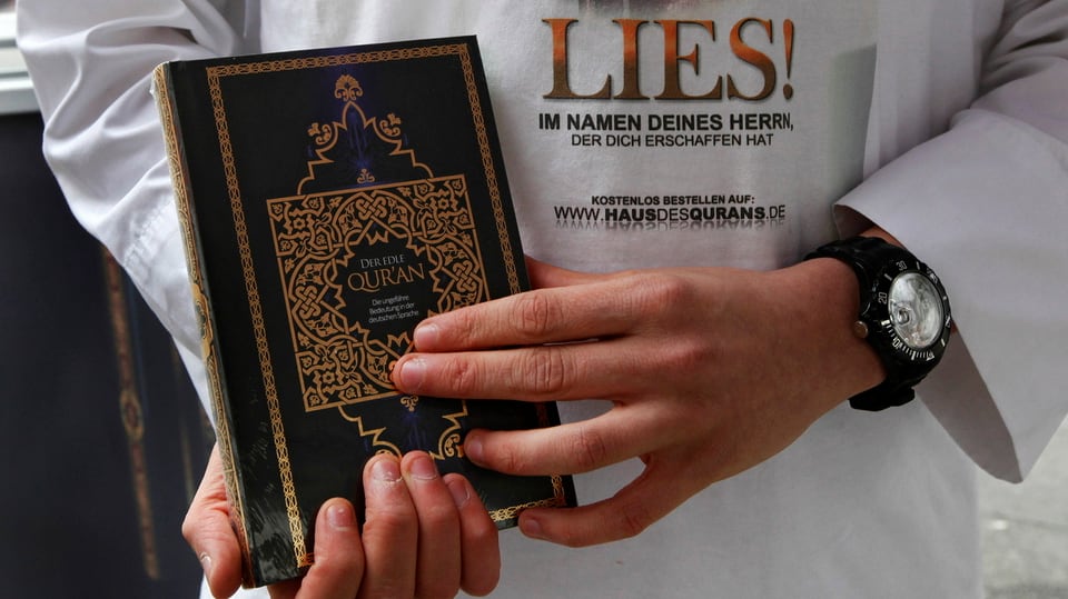 Eine Person hält einenKoran in den Händen, er trägt ein T-Shirt mit dem «Lies!»-Spruch.