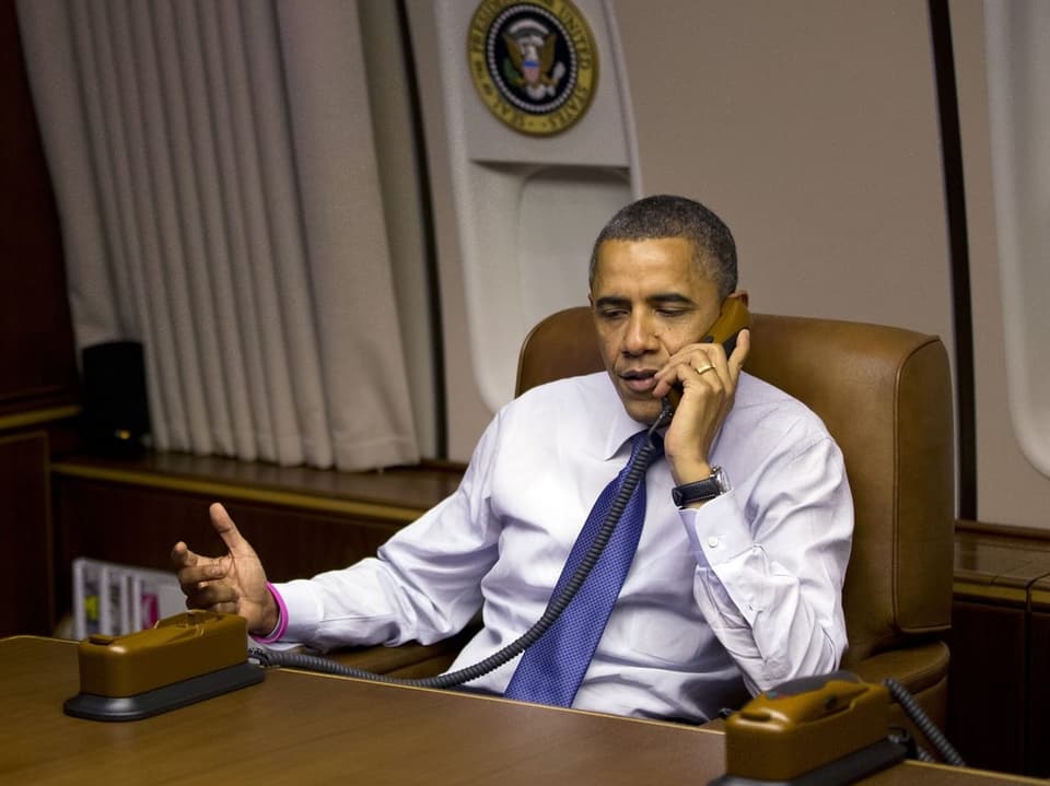 Obama sitzt am Tisch und telefoniert.