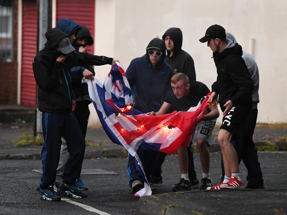 Schwarz gekleidete Jugendliche verbrennen auf der Strasse eine Union Jack-Flagge.