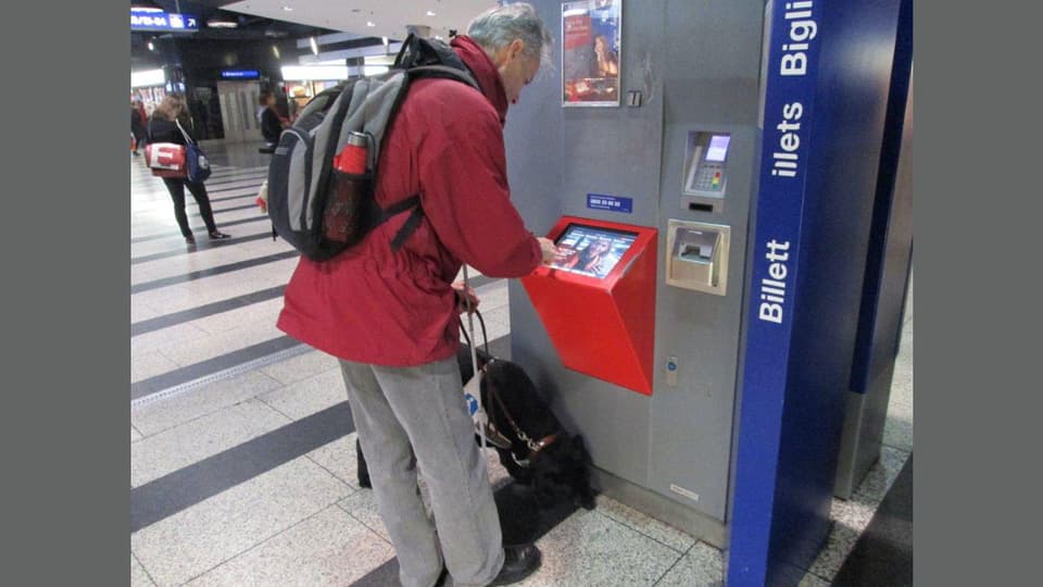 Ein blinder Mann versucht am Billettautomaten zurecht zu kommen.