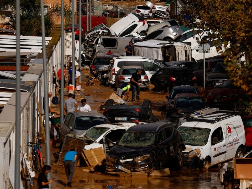 Überflutete Strasse mit gestapelten Autos und Menschen in schlammigem Wasser.