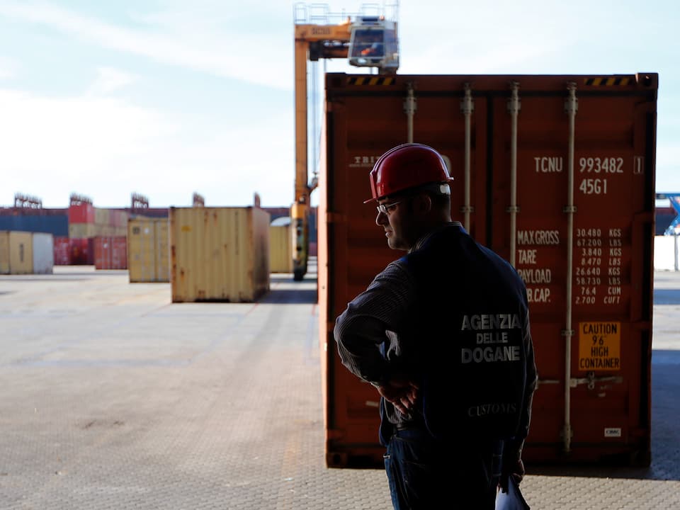 Ein Sicherheitsbeamter steht zwischen Containern am Hafen.