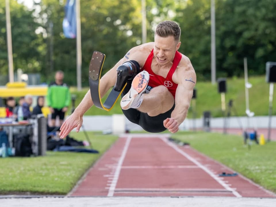 Sportler im Weitsprung mit Beinprothese in der Luft.