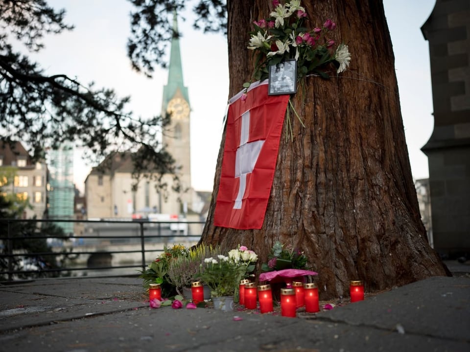 Blumen und Kerzen an einem Baum mit Schweizer Flagge.