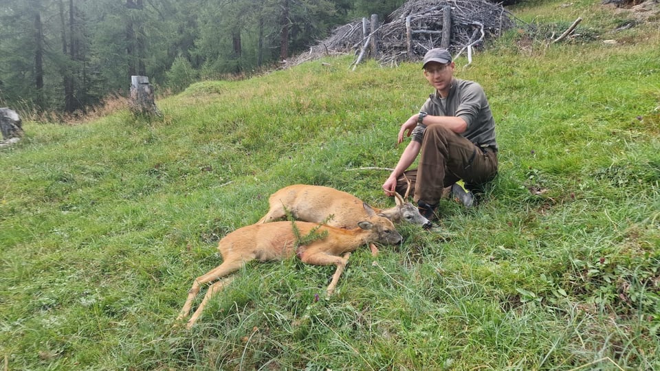 Jäger sitzt auf einer Wiese neben zwei erlegten Rehen.