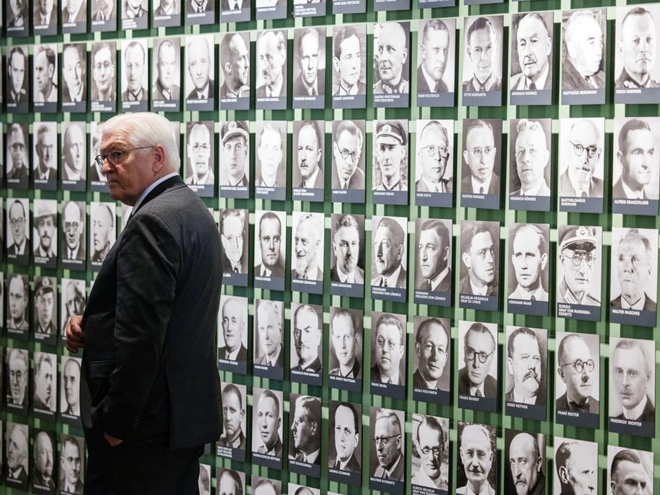 Mann betrachtet Wand voller Schwarz-Weiss-Porträts.
