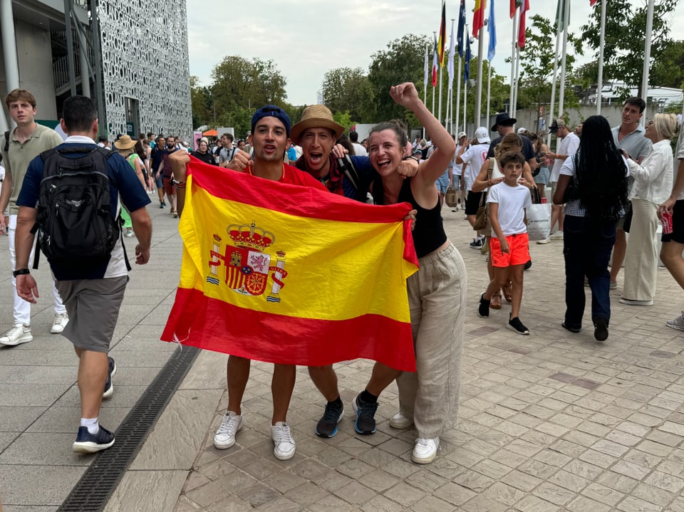 Drei Menschen halten eine spanische Flagge bei einer Veranstaltung.