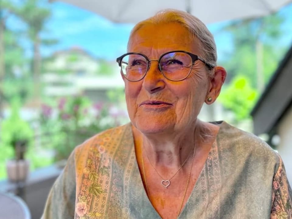 Ältere Dame mit Brille sitzt auf einem Balkon.