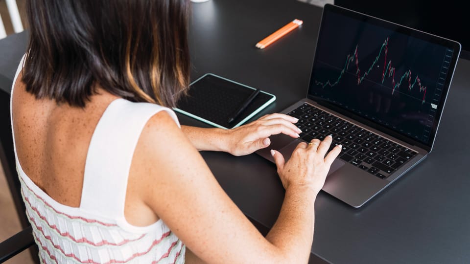 Frau mit dunklem haar von hinten an Laptop, darauf Aktienkurve zu sehen.