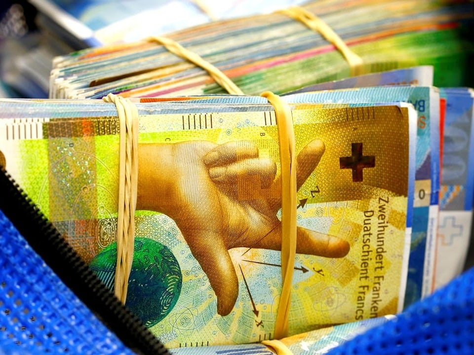 Eine blaue Tasche voll bepackt mit Bündeln aus Schweizer Banknoten.