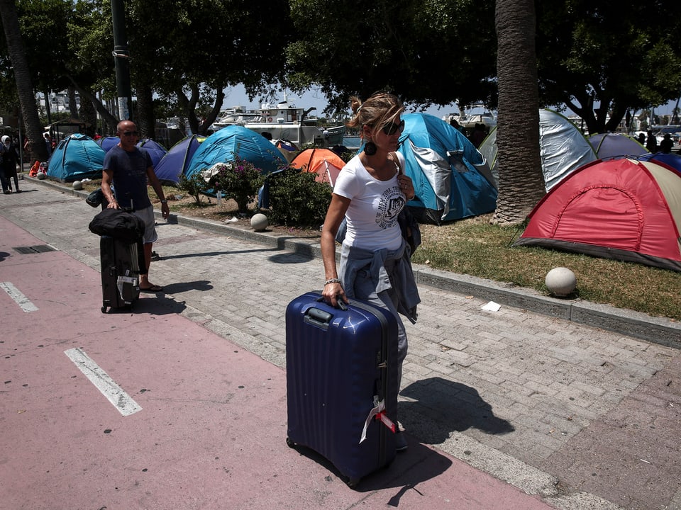 Touristen laufen an Zelten von Flüchtlingen vorbei.