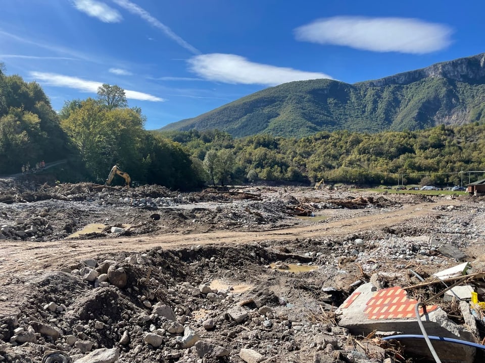 Baustelle in bergiger Landschaft mit Bagger und Trümmern.