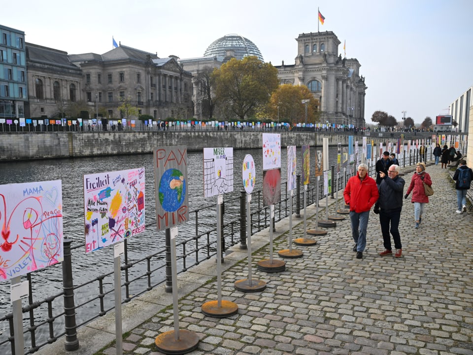 Menschenmenge auf einer Uferpromenade neben einer Brücke.