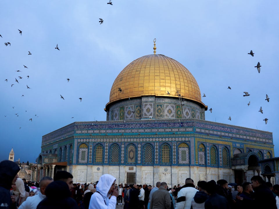 „Das Bild zeigt den Felsendom in Jerusalem bei Sonnenaufgang, umgeben von Menschen und Vögeln am Himmel.“