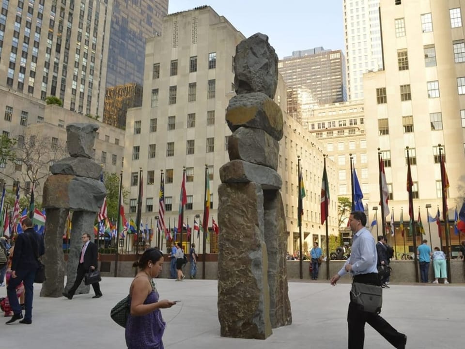 Menschen vor Felsenskulpturen auf einem städtischen Platz.
