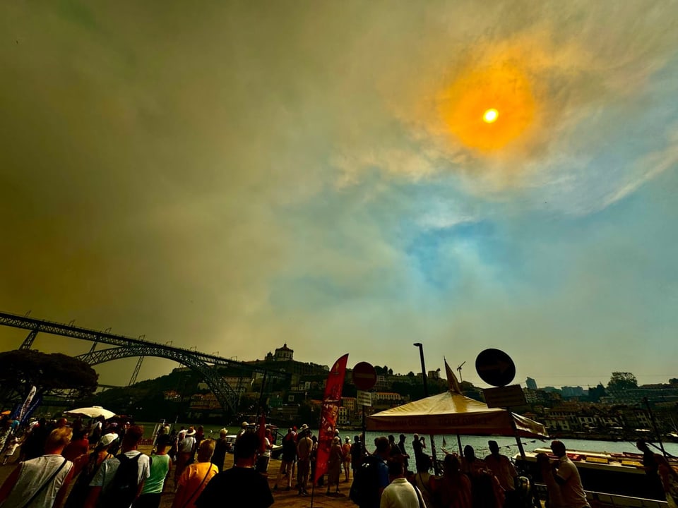 Menschenmenge unter einem düsteren, orangefarbenen Himmel mit einer hellen Sonne.