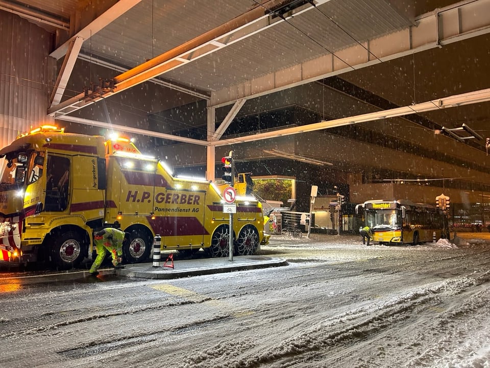 Abschleppwagen im Schnee vor Busstation bei Nacht.