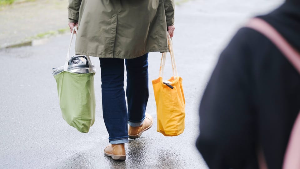 Person geht mit zwei Einkaufstaschen im Regen.