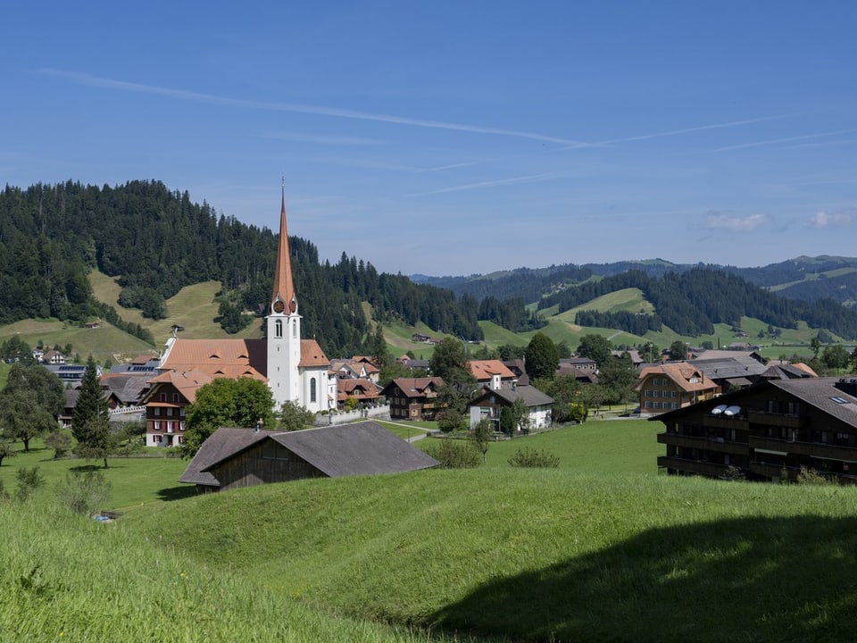 Idyllisches Dorf mit Kirche und Hügeln im Hintergrund.