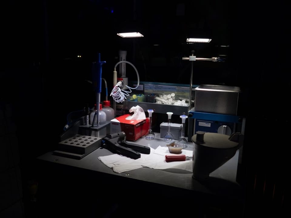 Laborarbeitstisch mit verschiedenen Geräten und Proben unter Lampenlicht.