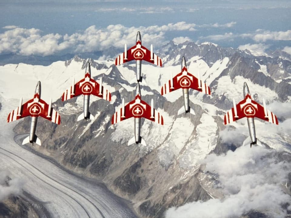 Sechs rot-weisse Flugzeuge fliegen über die schneebedeckten Alpen.