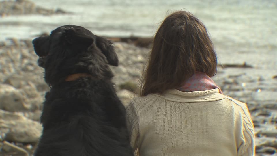 Frau und Hund von hinten, am See sitzend