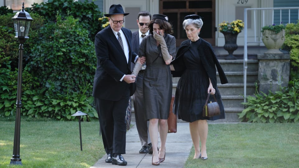 Anne Hathaway als trauernde Mutter mit anderen Besuchern der Beerdigung.