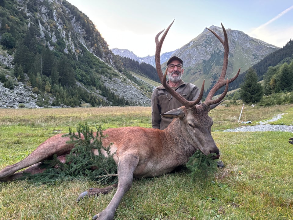 Mann posiert mit erlegtem Hirsch in den Bergen.