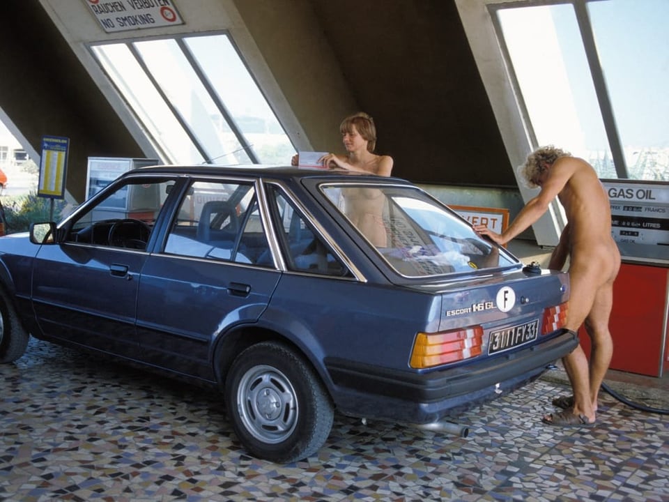 Zwei Männer neben einem Auto an einer Tankstelle.