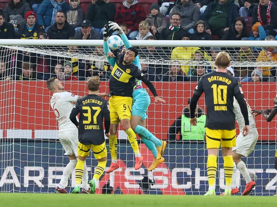 Fussballspiel mit Torwart in gelber Ausrüstung, der den Ball fängt.