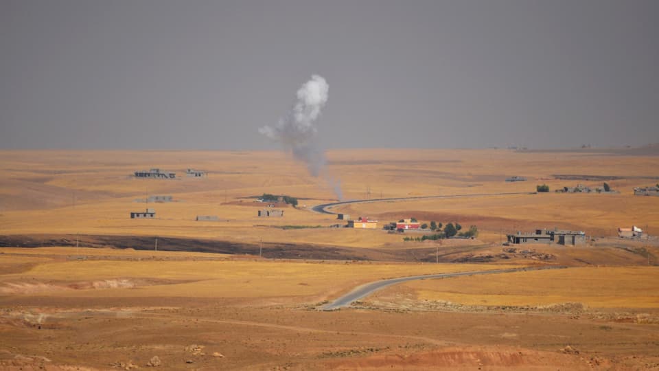 Wüstenähnliche Steppe, in der Ferne ein paar Häuser und eine aufsteigende Rauchwolke.