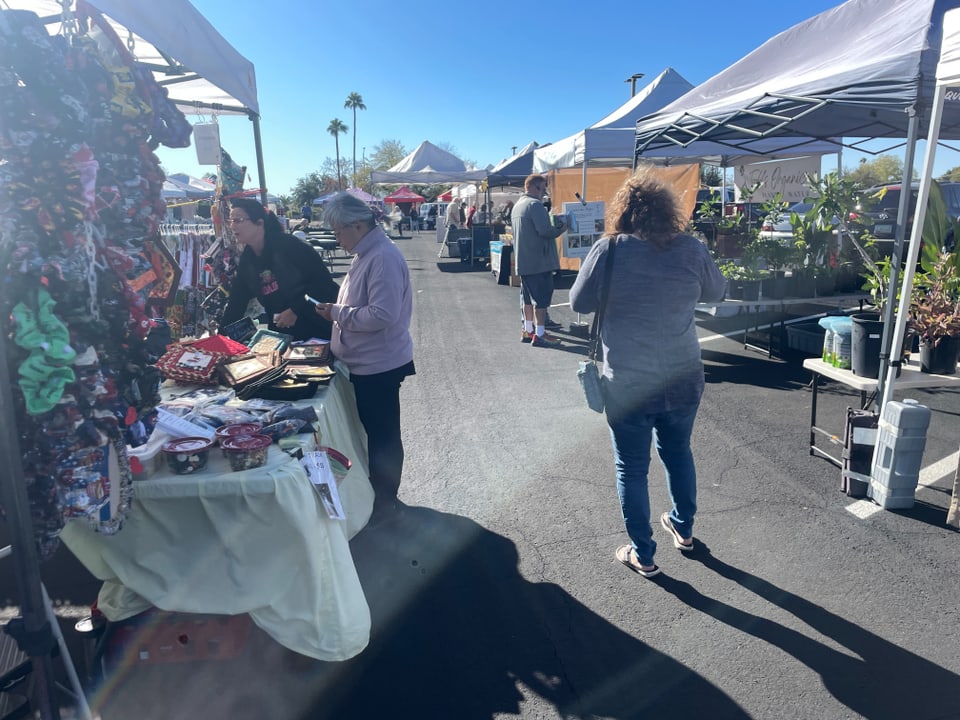 Personen auf einem sonnigen Markt mit Ständen und Pflanzen.