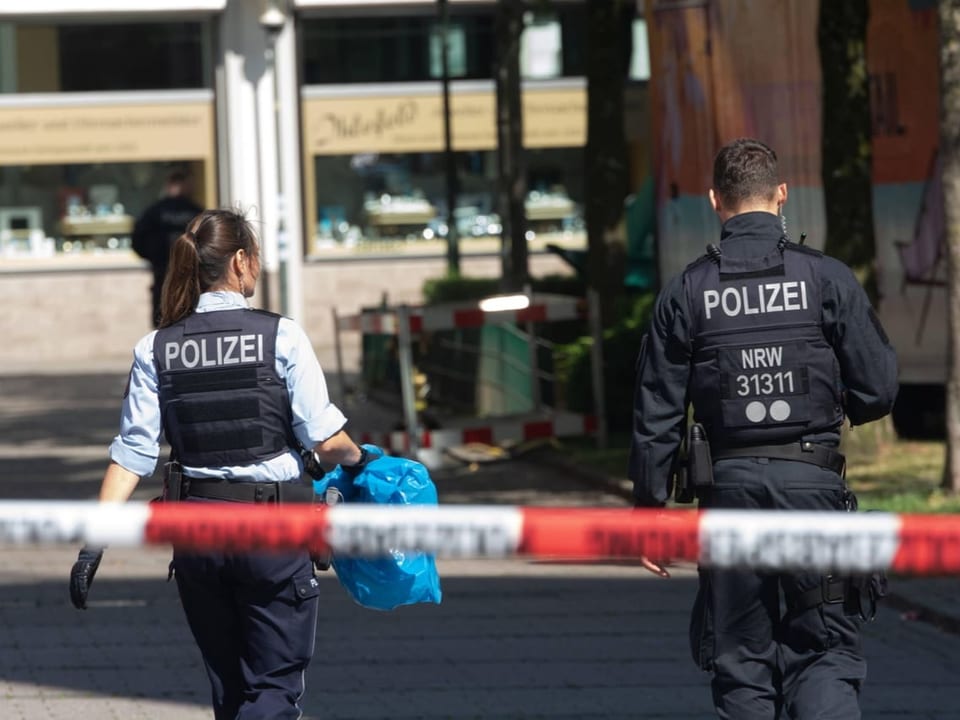 Zwei Polizisten in Einsatzkleidung hinter Absperrband.