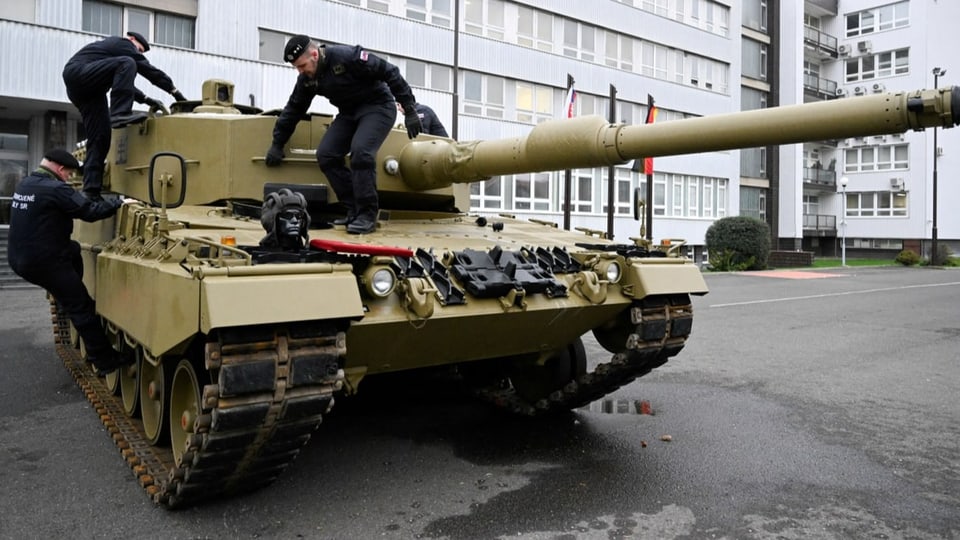 Ein sandfarbener Panzer Leopard wird von Mechanikern inspiziert.