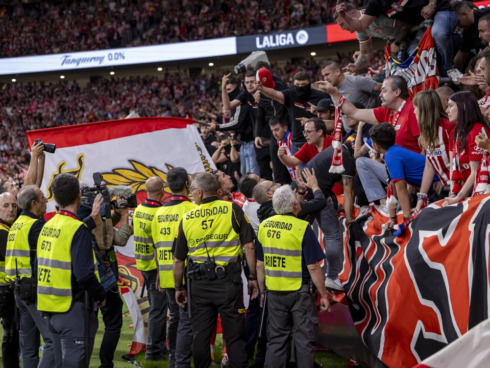 Sicherheitskräfte und Fussballfans im Stadion feiern mit einer Fahne.