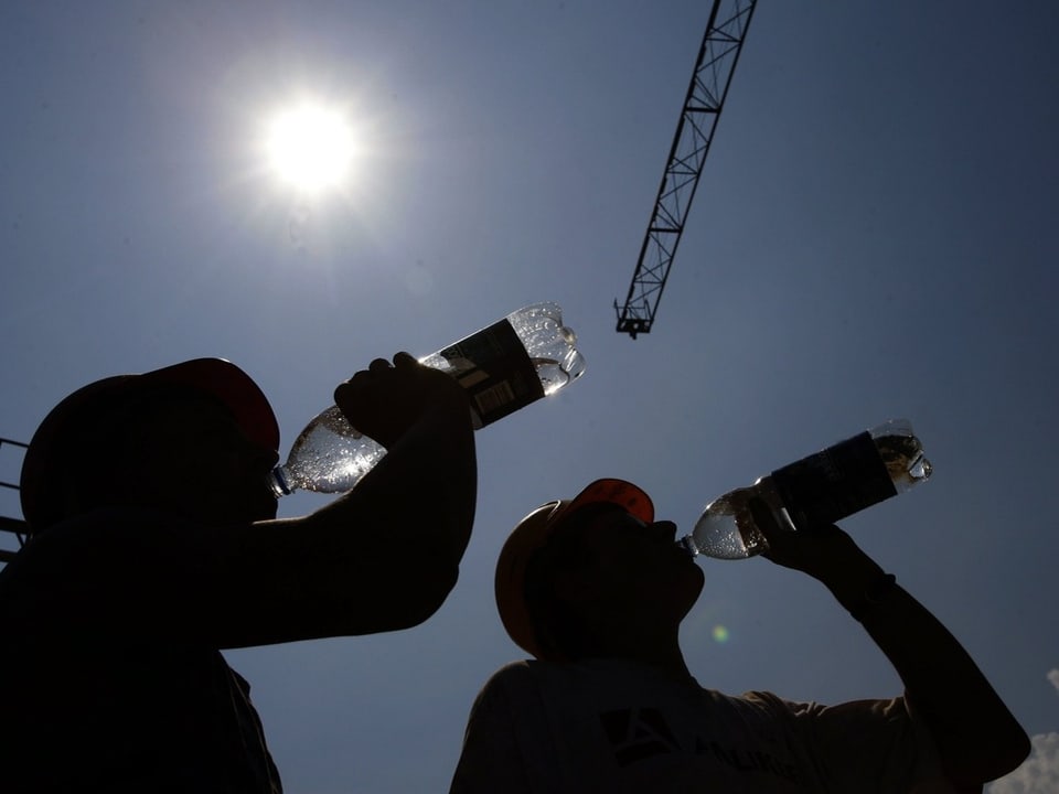 Silhouetten von Bauarbeitern, die Wasser trinken, vor hellem Himmel mit Sonnenlicht und Kran.