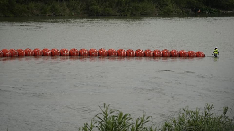orangefarbene, schwimmende Bojen angereiht auf einem Fluss