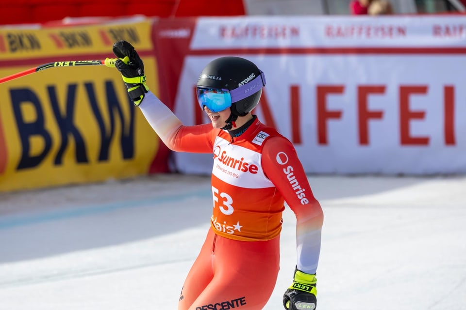 Skifahrerin im roten Rennanzug jubelt mit erhobenem Stock.