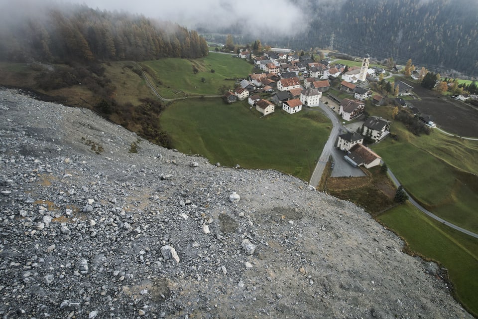 Blick auf ein Dorf am Hang unter einer Wolkendecke.