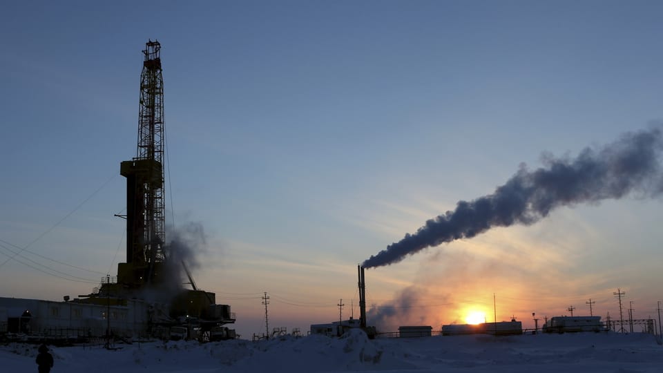 Ölbohrturm udn rauchender Schlot im Schnee bei Sonnenaufgang.