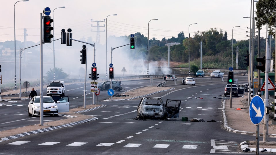 Verkehrskreuzung in Sderot mit ausgebranntem Auto und Rauch im Hintergrund.