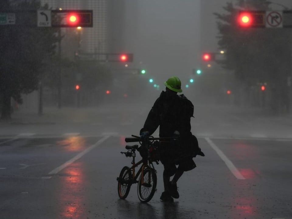 Person mit Fahrrad im Regen auf leerer Stadtstrasse.