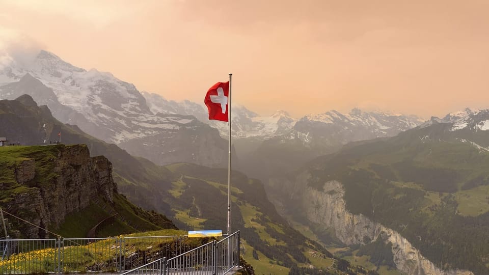 Schweizer Flagge auf einer Bergplattform mit Alpen im Hintergrund.