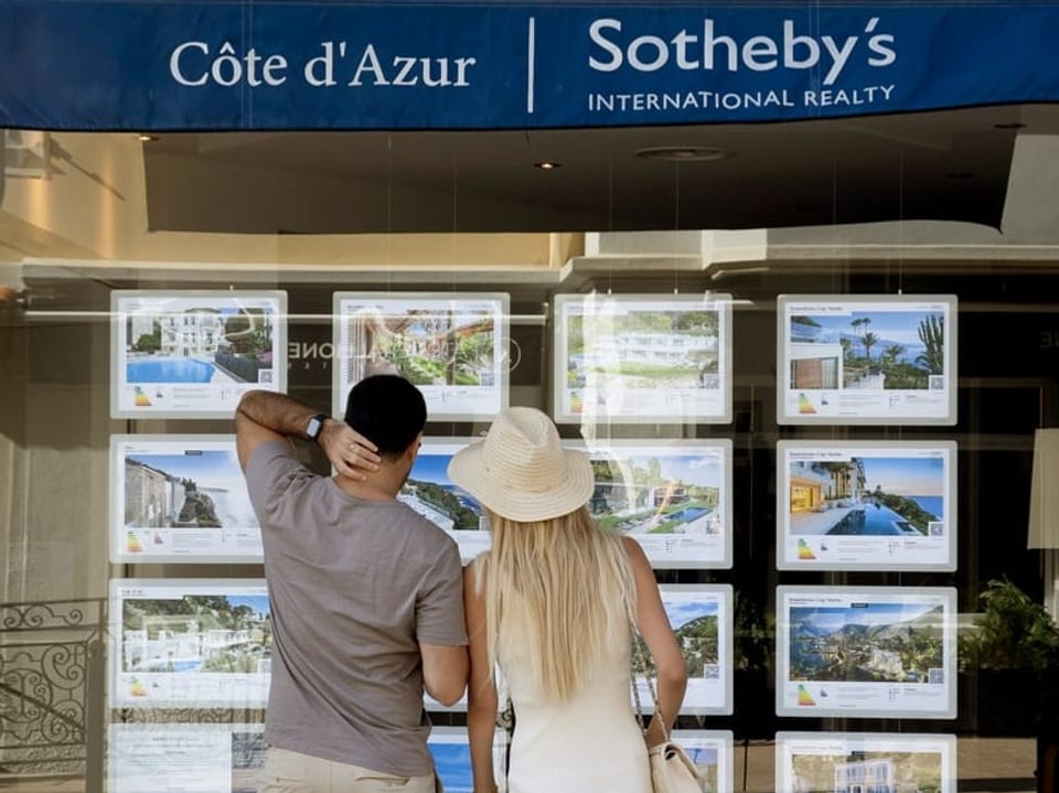 Zwei Personen betrachten Immobilienanzeigen im Sotheby's Schaufenster.