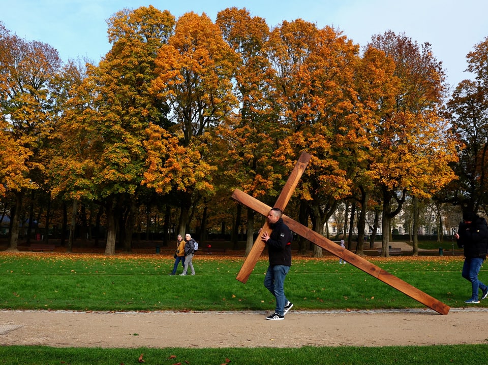 Mann trägt grosses Holzkreuz im Park im Herbst.