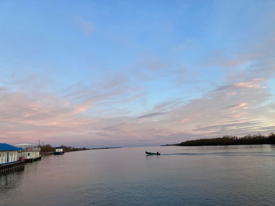 Boot auf ruhigem Fluss bei Sonnenuntergang, Pastellhimmel.