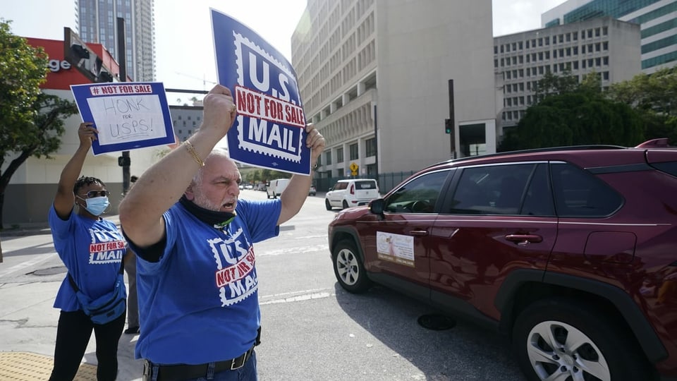 Zwei Personen demonstrieren mit Schildern gegen Änderungen bei der US-Post.