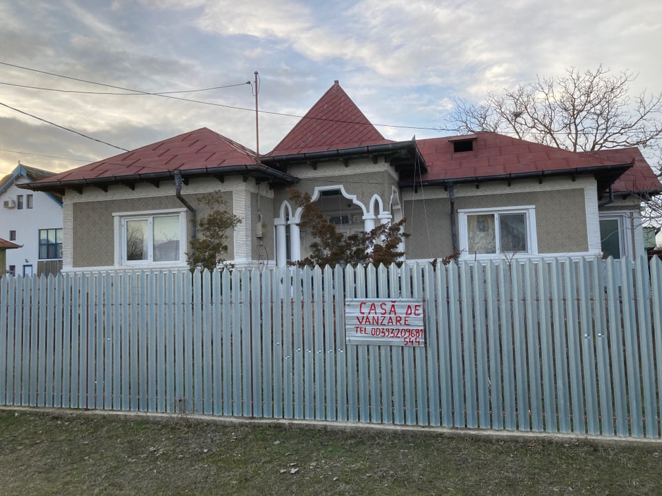 Einfamilienhaus mit Verkaufsschild hinter einem Holzzaun.